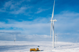 a wind turbine sat against a snowy landscape with a much smaller truck for scale