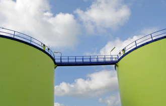 two green storage tanks pictured against a blue sky