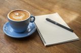 a notepad and pen sitting next to a cup of coffee in a blue cup and saucer