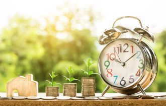 piles of money siting alongside an alarm clock with plants in the background