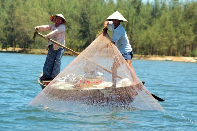 two Vietnamese fisherman fishing in a traditional manner