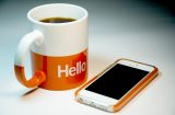 a white and orange mug with hello written on it next to an iphone
