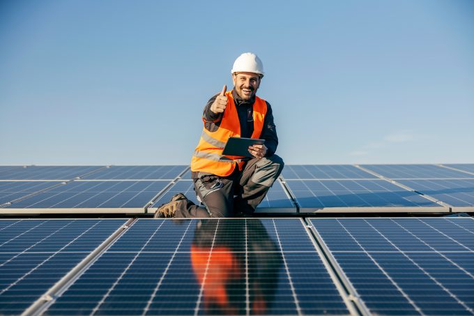 A,Worker,On,Rooftop,Kneeling,Next,To,Solar,Panels,With