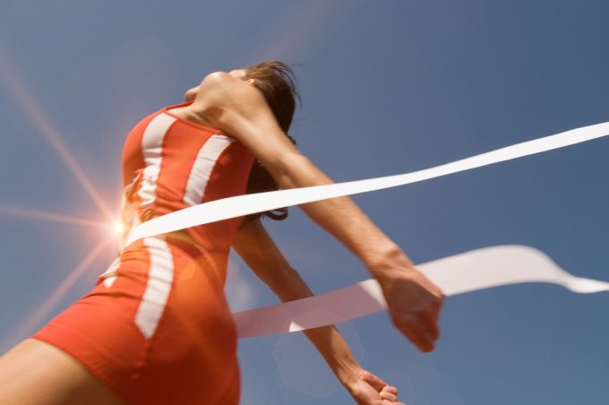 Low,Angle,View,Of,Young,Female,Athlete,Crossing,Finish,Line