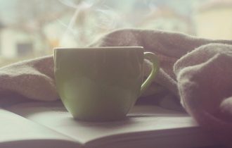 a green cup of something hot - tea or coffee? - sitting on an open bookon which is also resting what looks like a napkin 230406 morning
