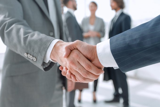 two men in suits shaking hands against a blurred backdrop of other people in business attire