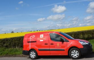a red royal mail van driving past a yellow field on a sunny day