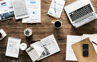 a desk covered with notebooks, a laptop, a calculator, a cup of coffee
