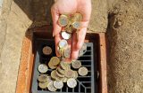 a hand throwing pound coins into a drain