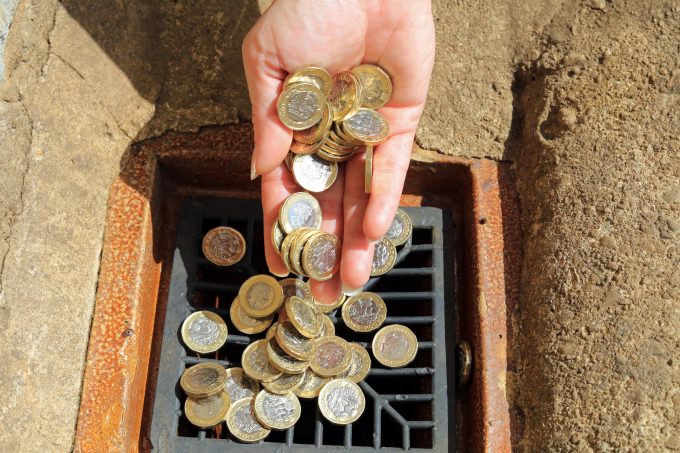 a hand throwing pound coins into a drain