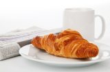a newspaper, a croissant and a mug of tea or coffee
