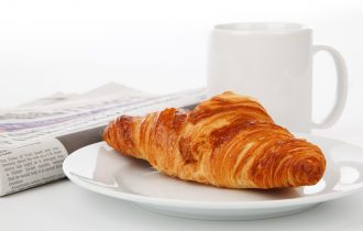 a newspaper, a croissant and a mug of tea or coffee