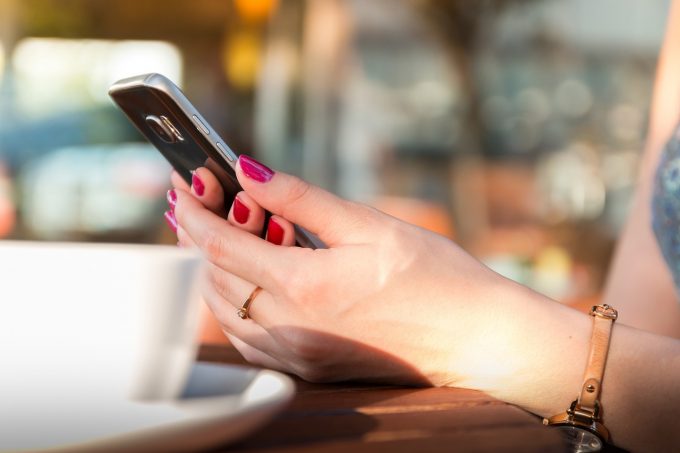 hands holding a phone beside a cup