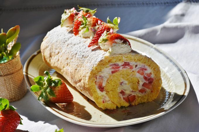 a strawberry roll on a plate next to some whole strawberries
