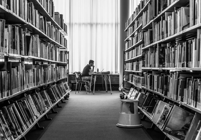 a student studies in a library - view through two rows of books of a student at a desk