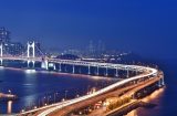 a view of the Gwangan Bridge in Busan South Korea at night - a suspension bridge crosses a body of water towards a city in the distance