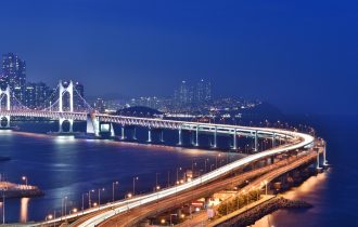 a view of the Gwangan Bridge in Busan South Korea at night - a suspension bridge crosses a body of water towards a city in the distance
