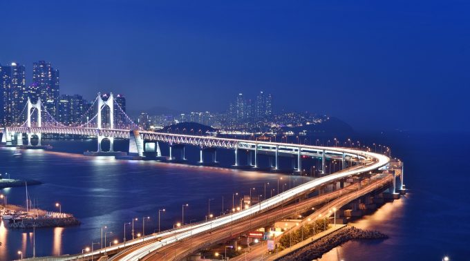 a view of the Gwangan Bridge in Busan South Korea at night - a suspension bridge crosses a body of water towards a city in the distance