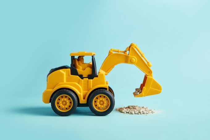 a yellow toy digger on a light blue background looks to be picking up a pile of grey dust
