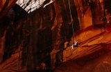 someone on a safety harness dangling from a rop in a canyon of red rocks