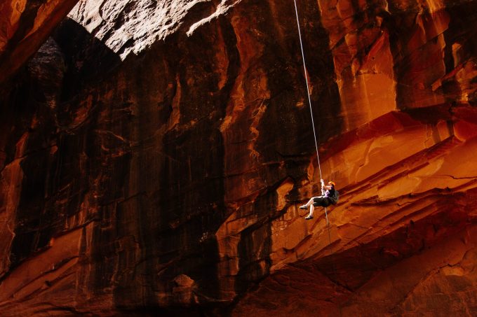 someone on a safety harness dangling from a rop in a canyon of red rocks