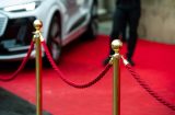 a velvet rope infront of a red carpet with the edge of a luxury car in the corner
