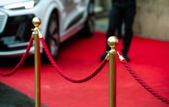 a velvet rope infront of a red carpet with the edge of a luxury car in the corner