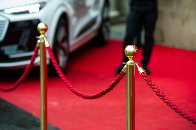 a velvet rope infront of a red carpet with the edge of a luxury car in the corner